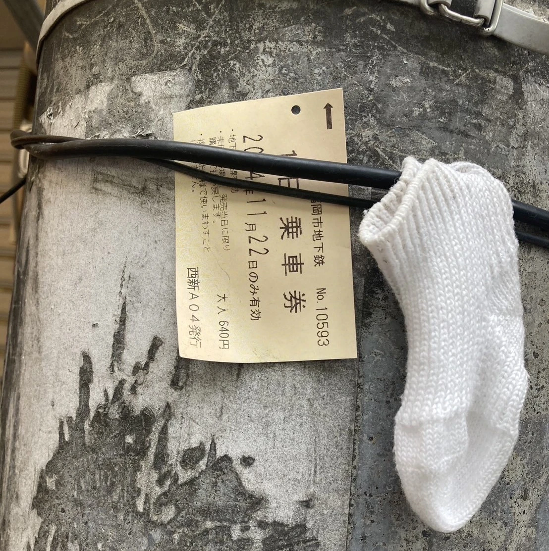 地下鉄の一日乗車券と白い靴下を、誰かが電柱に挟んでいる
